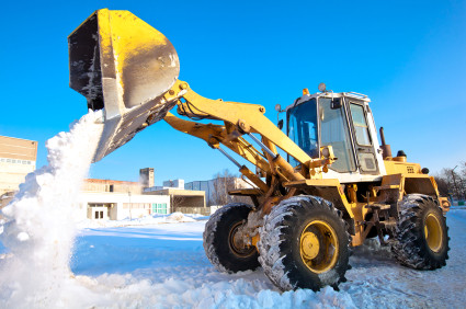 A big yellow bulldozer removes snow from parking lot.